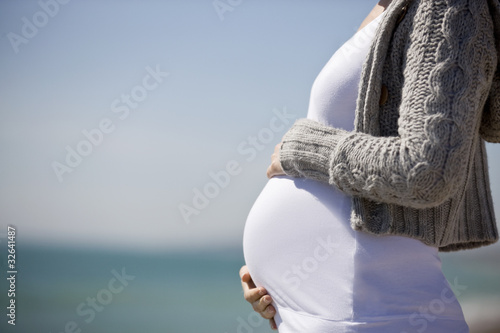 Photo: A pregnant woman standing on the beach, holding her belly A pregnant woman standing on the beach, holding her belly