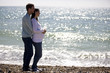 A pregnant woman and her partner embracing on the beach