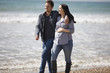 A pregnant woman and her partner walking on the beach