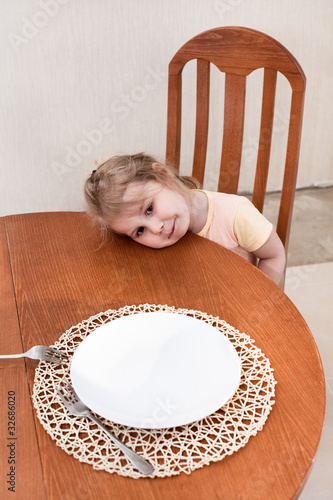 Photo: Little child sitting along at table with empty plate Little child sitting along at table with empty plate