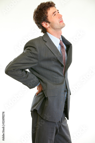 Photo: Young businessman holding hand at his aching back Young businessman holding hand at his aching back