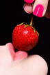 Photo: Closeup of young woman full lips with strawberry against black Closeup of young woman full lips with strawberry against black