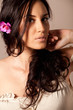 Portrait of young brunette woman with flower in curly hair