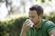 A young man outdoors, sneezing