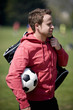 A young man carrying a football and a sports bag