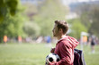 A young man standing in the park, carrying a football