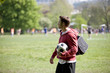 A young man standing in the park, carrying a football
