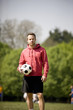 A young man standing in the park, holding a football