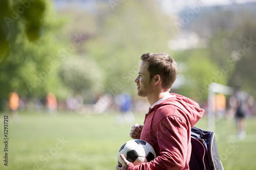 Photo: A young man standing in the park, carrying a football A young man standing in the park, carrying a football