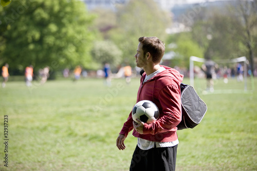Foto: A young man standing in the park, carrying a football A young man standing in the park, carrying a football