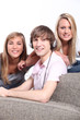a boy listening music and two blonde girls behind a couch
