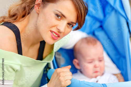 Photo: Caring young mother hugging sitting in stroller crying baby. Caring young mother hugging sitting in stroller crying baby.