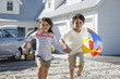 Brother and sister with beach ball running on driveway
