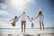 Family holding hands and jumping on beach