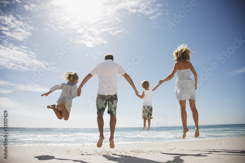 Photo: Family holding hands and jumping on beach Family holding hands and jumping on beach