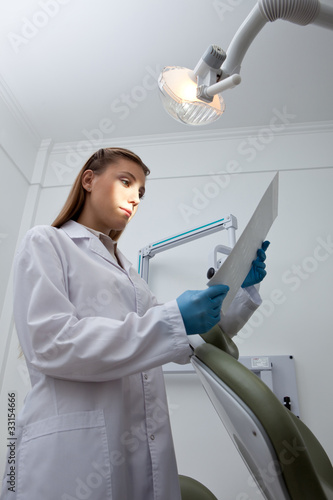 Foto: Dentist standing at dentist's chair under lamp Dentist standing at dentist's chair under lamp