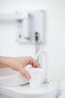 Hand holding plastic beaker at faucet in dentist's office