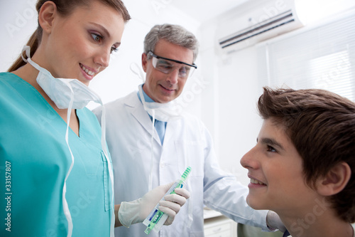 Photo: Dentist's assistant holding toothbrush and toothpaste talking to boy Dentist's assistant holding toothbrush and toothpaste talking to boy