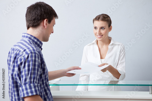 Photo: Receptionist passing document to man Receptionist passing document to man