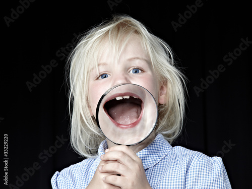 Photo: Blond girl laughing with magnifier in front of her open mouth Blond girl laughing with magnifier in front of her open mouth
