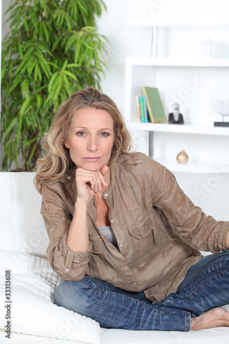 Photo: Serious woman sitting crossed legged on a white sofa Serious woman sitting crossed legged on a white sofa