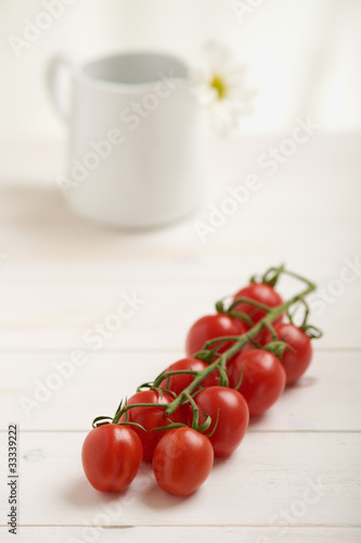 Photo: Cherry tomatoes on a white table, white flower in background Cherry tomatoes on a white table, white flower in background
