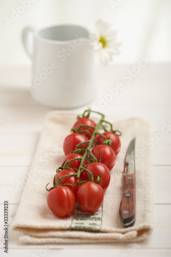 Photo: Cherry tomatoes on a white table, white flower in background Cherry tomatoes on a white table, white flower in background