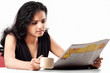 Smiling indian teen reading newspaper with coffee