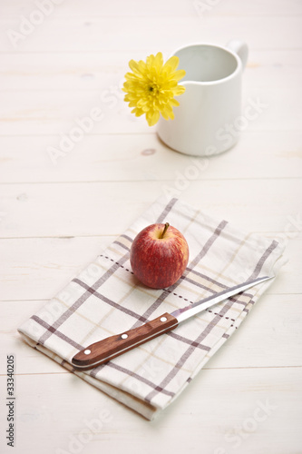 Photo: red apple on a white table, in backgroiund a flower red apple on a white table, in backgroiund a flower