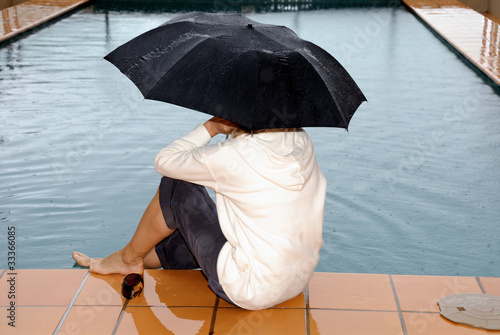 Photo: Frau sitzt am Schwimmbad im Regen Frau sitzt am Schwimmbad im Regen