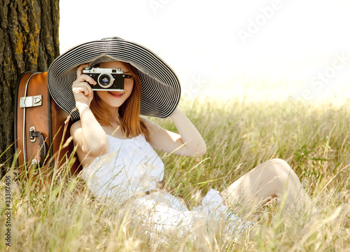 Photo: Redhead girl sitting near tree with vintage camera. Redhead girl sitting near tree with vintage camera.