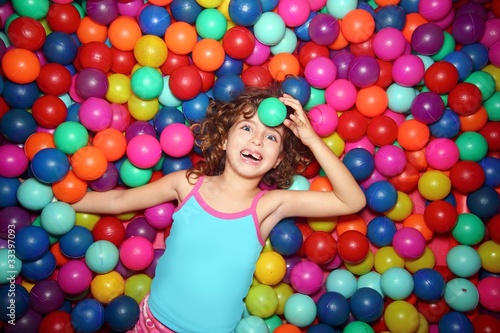 Photo: little girl playing lying in colorful balls park playground little girl playing lying in colorful balls park playground
