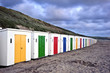 Row of colorful beach huts receding into distance on empty beach
