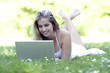Foto: Junge Frau liegt mit einem Laptop auf einer Wiese Junge Frau liegt mit einem Laptop auf einer Wiese