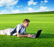 Young man use a notebook on green field
