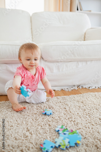 Photo: Lovely blond baby playing with puzzle pieces while sitting on a Lovely blond baby playing with puzzle pieces while sitting on a