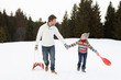 Young Father And Daughter Walking In Snow With Sleds