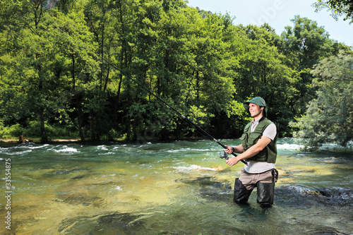Photo: Fisherman fishing on a river with forest in the background Fisherman fishing on a river with forest in the background
