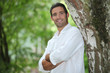 Man standing with his arms crossed under a large tree