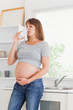 Good looking pregnant woman holding a glass of water while stand