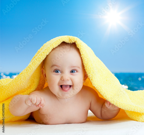Photo: Adorable happy baby in colorful towel on sea beach Adorable happy baby in colorful towel on sea beach