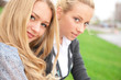 Two women hugging and smiling sitting on the grass at city park