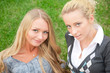 Two women hugging and smiling sitting on the grass at city park