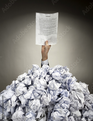 Photo: Hand with agreement reaches out from heap of papers Hand with agreement reaches out from heap of papers