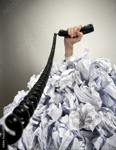 Photo: Hand with phone reaches out from heap of papers Hand with phone reaches out from heap of papers