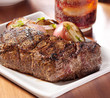 grilled steak with potatoes and cola in background.