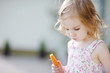 Adorable happy preschooler girl eating carrot outdoors