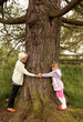 Oma und Enkelin umarmen einen grossen Baum