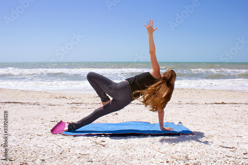 Photo: woman doing yoga exercise on beach in Vasisthasana or side plank woman doing yoga exercise on beach in Vasisthasana or side plank