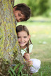 Two little children hiding behind tree